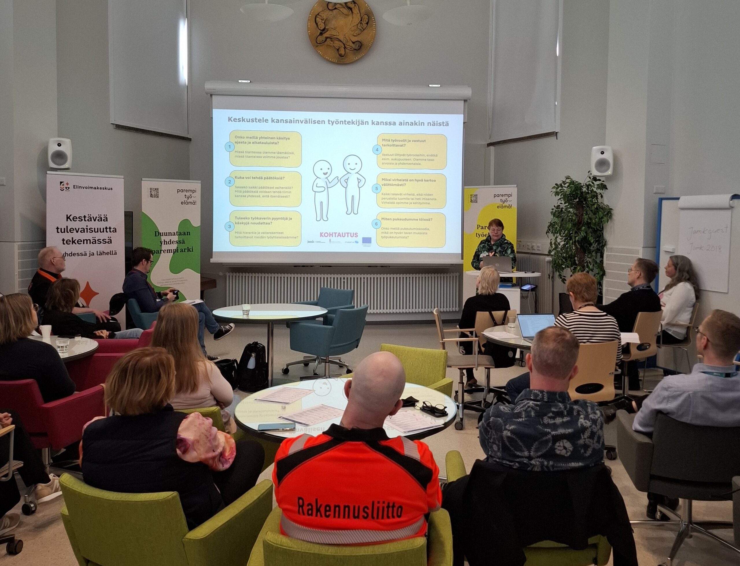 Kuva Jyväskylän Paremman työelämän tekijät tapahtumasta, jossa on ihmisiä katselemassa esiintyjää ja diaesitystä.